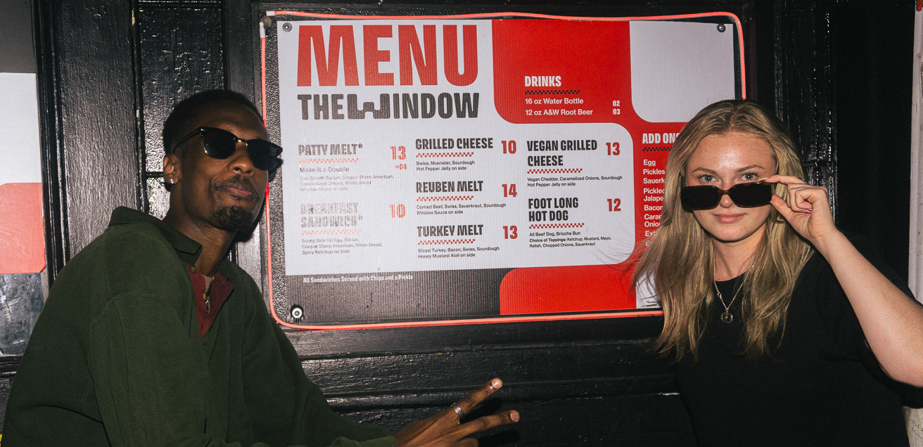 Two customers posing in front of the store menu.